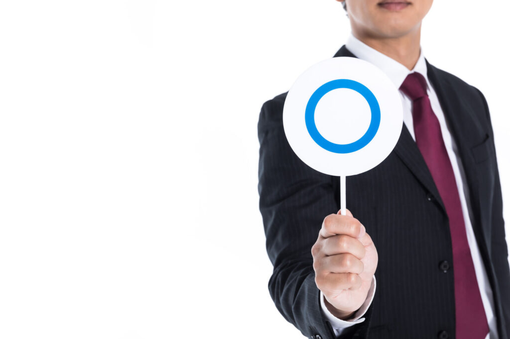 ◯マークをこちらに向けるスーツの男性